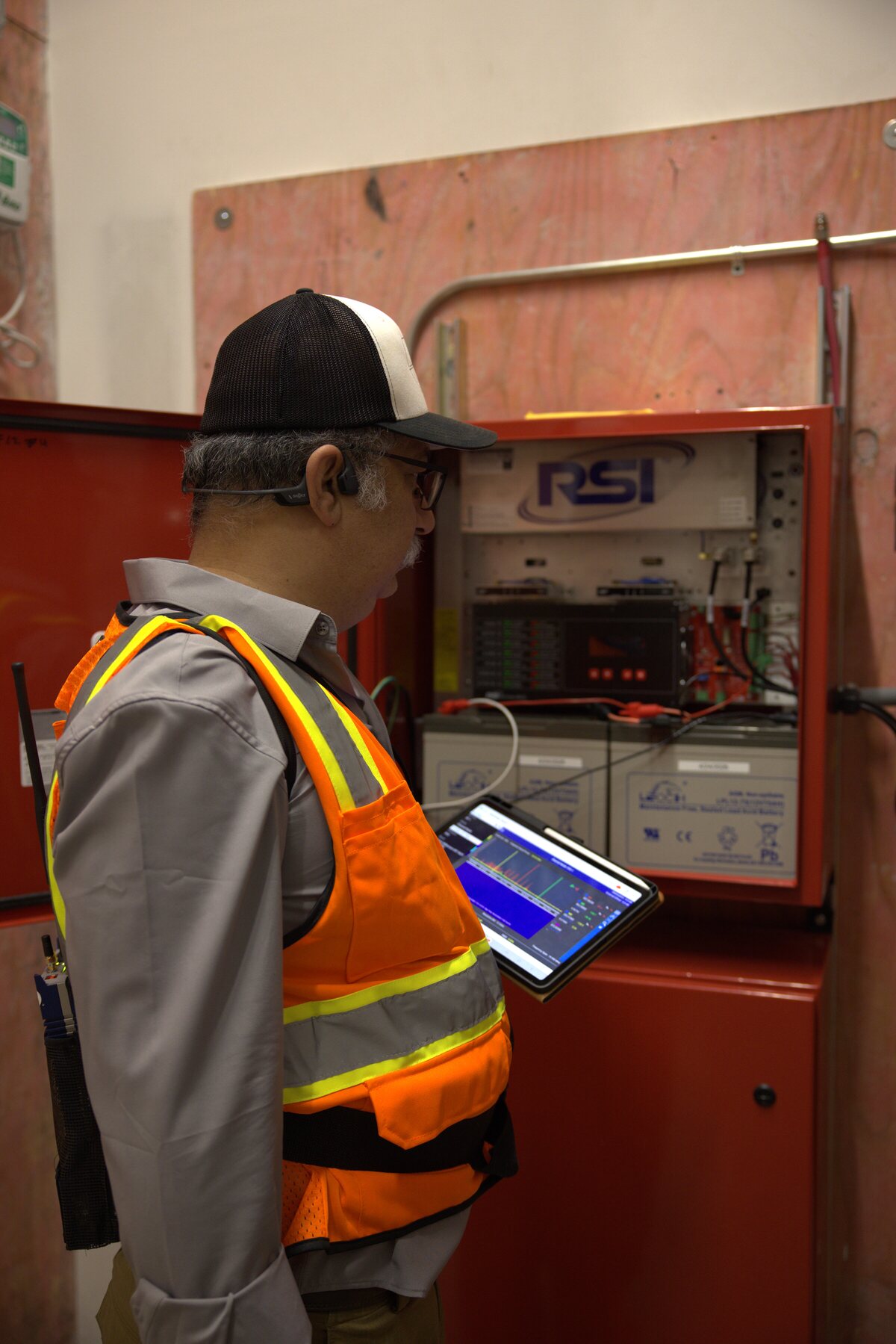 Zion technician reviewing live signal data on a tablet in front of an RSI ERCES / BDA head-end cabinet — UL 2524 amplifier with dedicated backup batteries during acceptance testing at a Texas commercial building